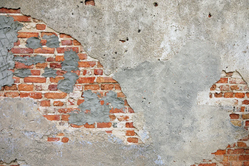Damaged wall with patches of failed plaster and exposed brickwork awaiting repair